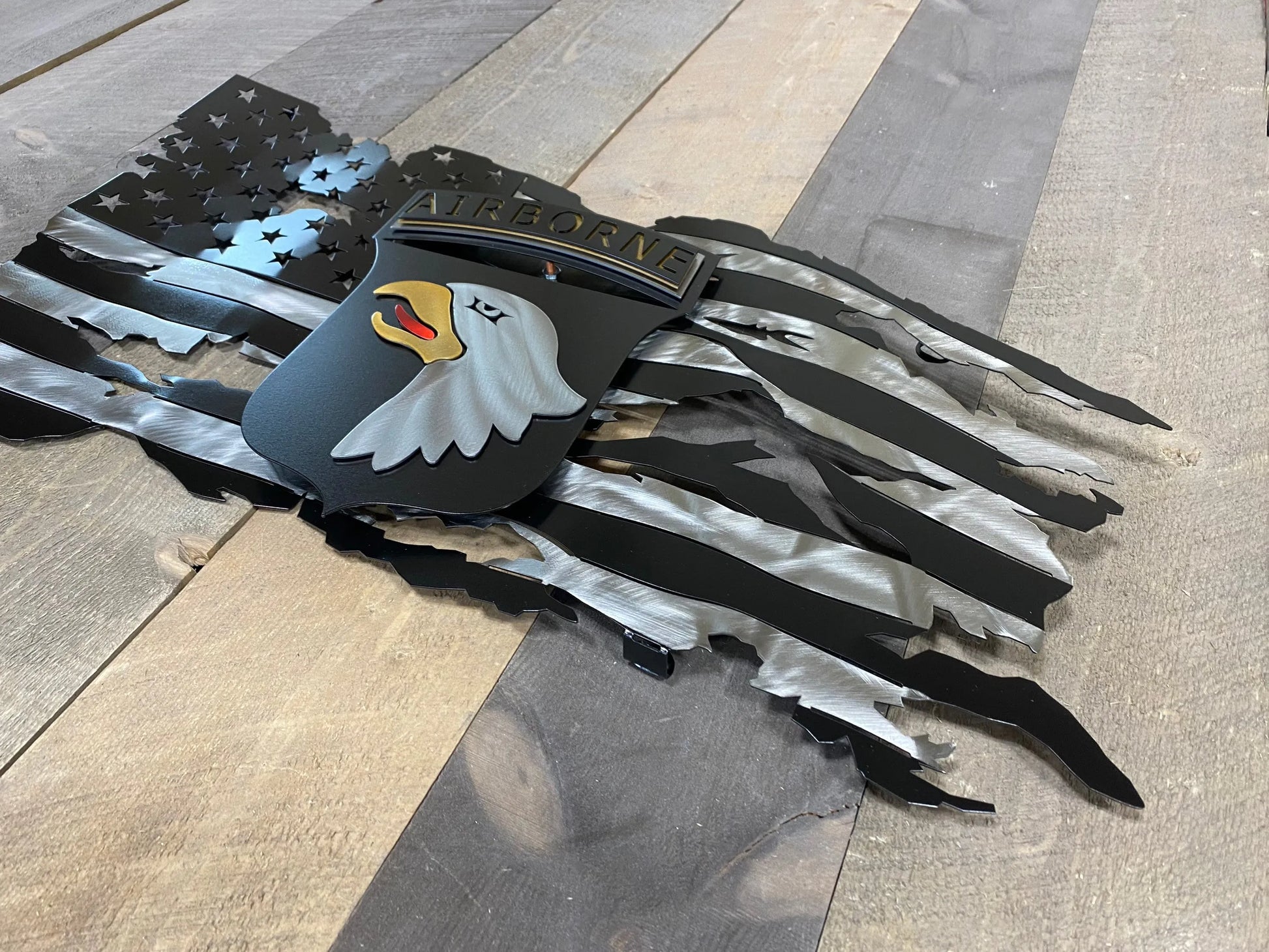 Tattered metal American flag featuring the 101st Airborne Division emblem in black and silver.