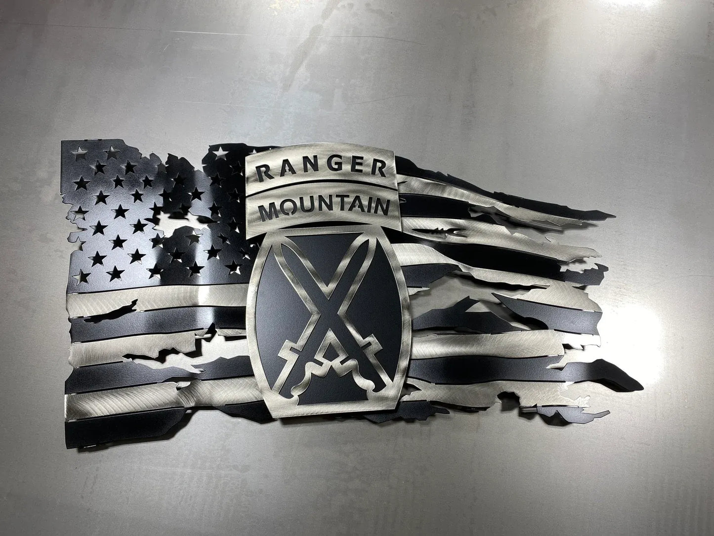 Tattered metal American flag featuring the 10th Mountain Division Ranger emblem in black and silver.