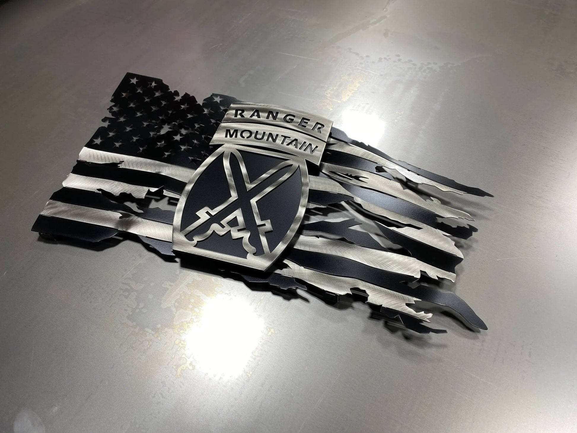 Tattered metal American flag featuring the 10th Mountain Division Ranger emblem in black and silver.
