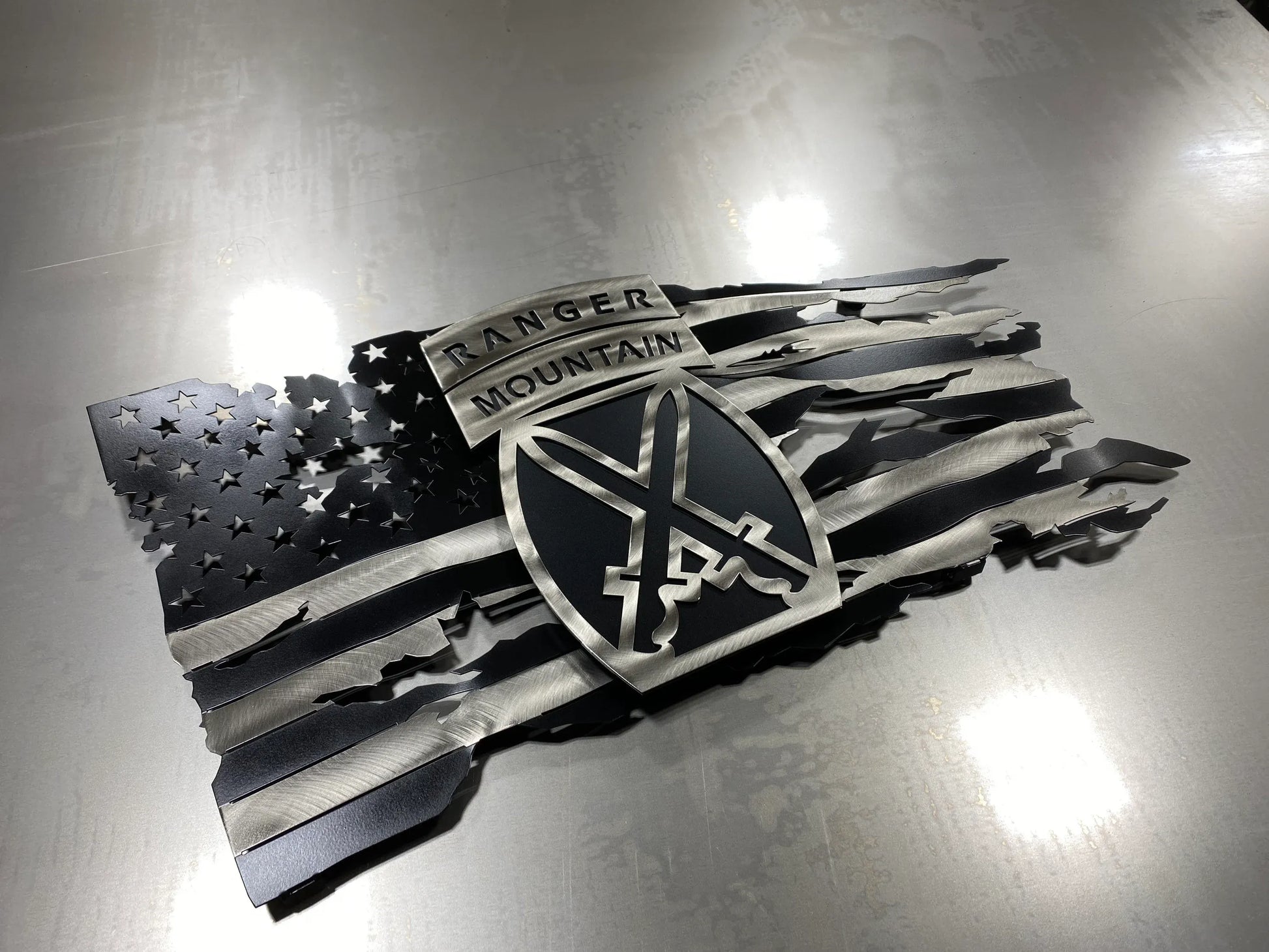 Tattered metal American flag featuring the 10th Mountain Division Ranger emblem in black and silver.