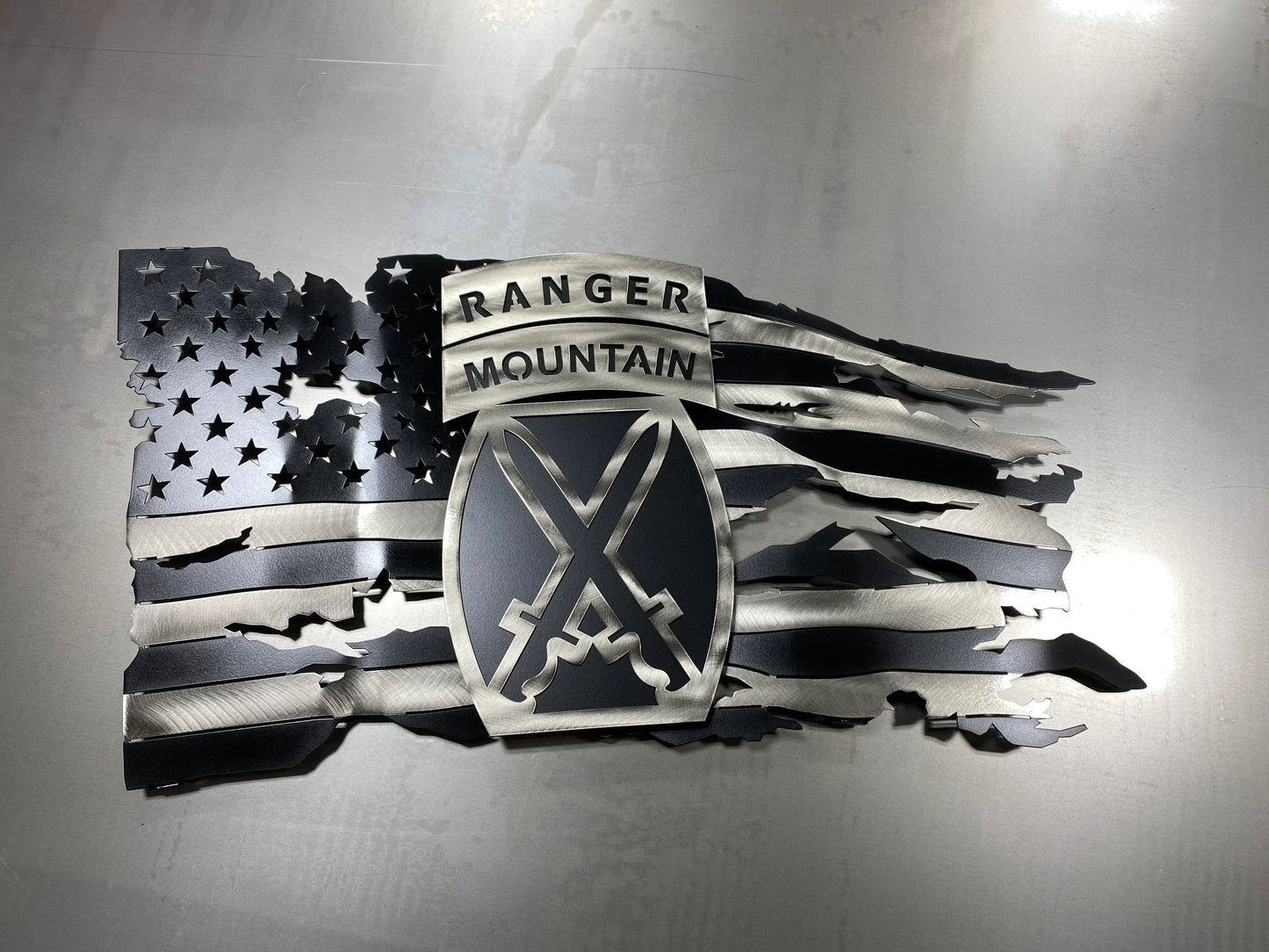 Tattered metal American flag featuring the 10th Mountain Division Ranger emblem in black and silver.