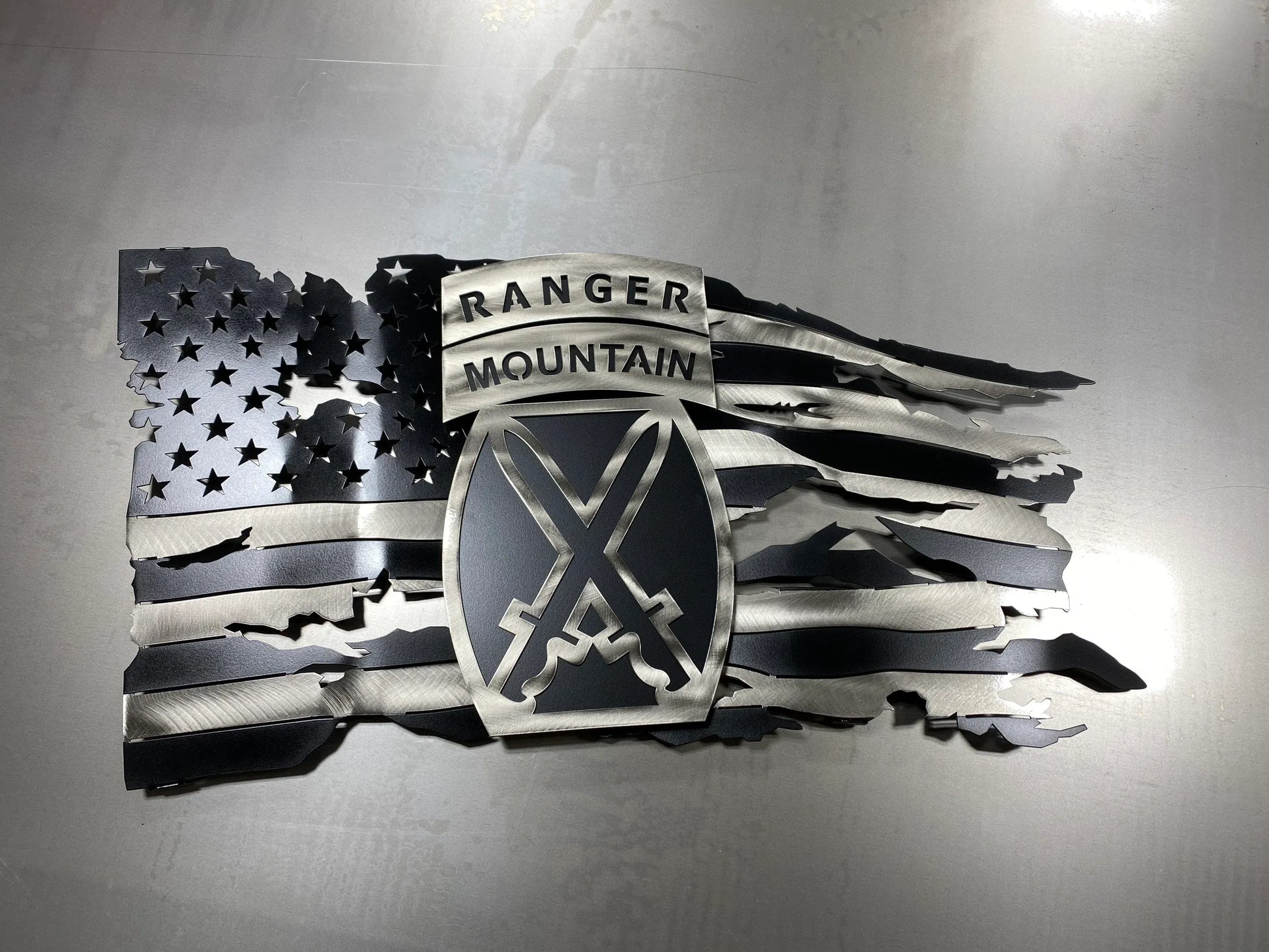 Tattered metal American flag featuring the 10th Mountain Division Ranger emblem in black and silver.